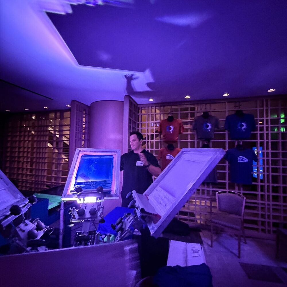 Finished custom merch displayed on a wall grid under purple event lighting
